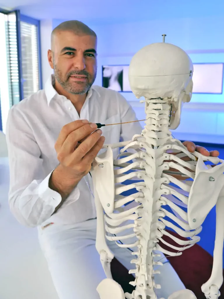 Dr. Ismail zeigt mit Sonde auf Halswirbel